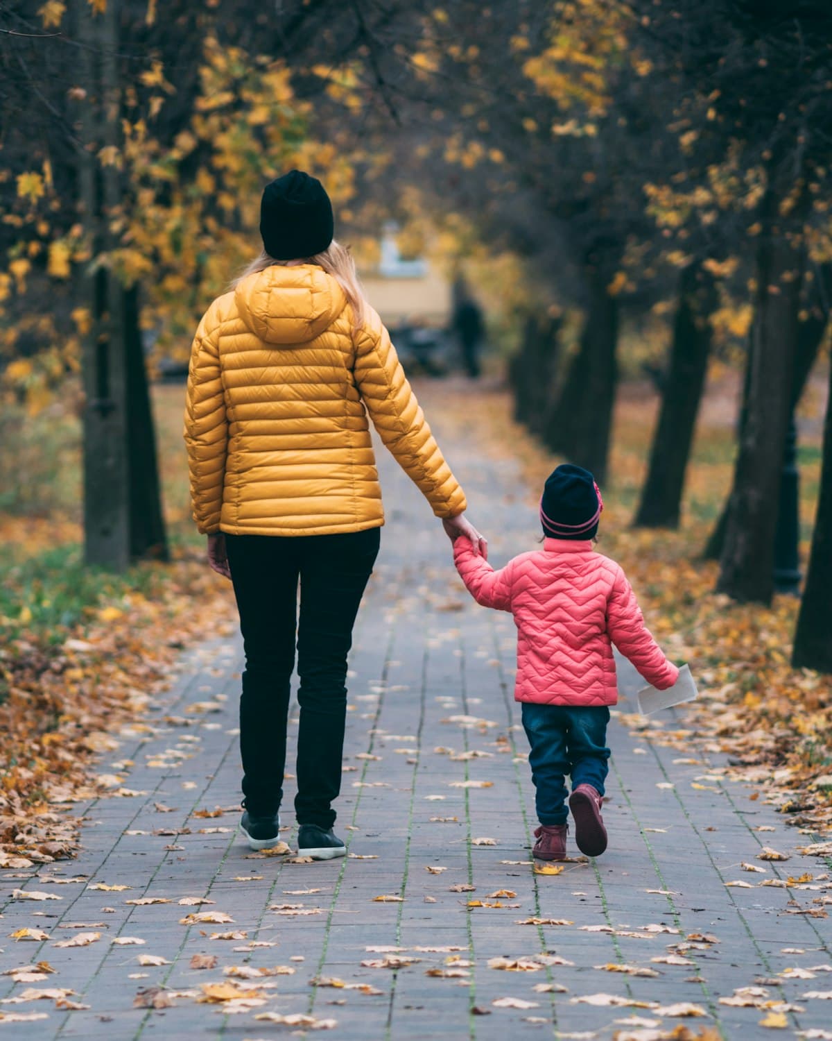 Eine Mutter geht mit ihrem Kind an der Hand durch eine herbstliche Allee